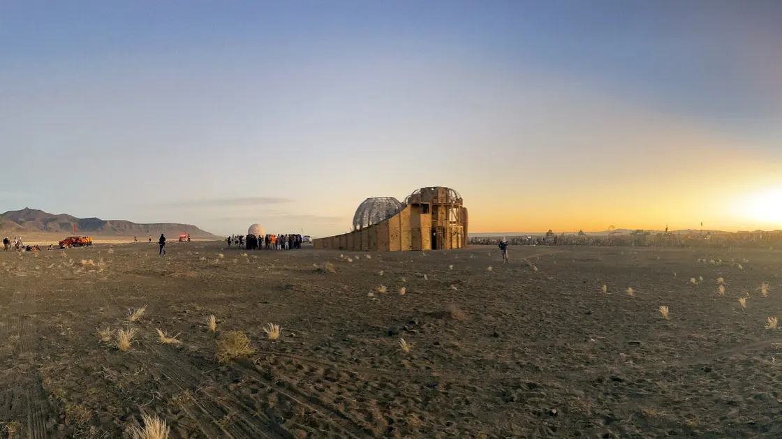 A flat desert plain at dusk with a distant structure