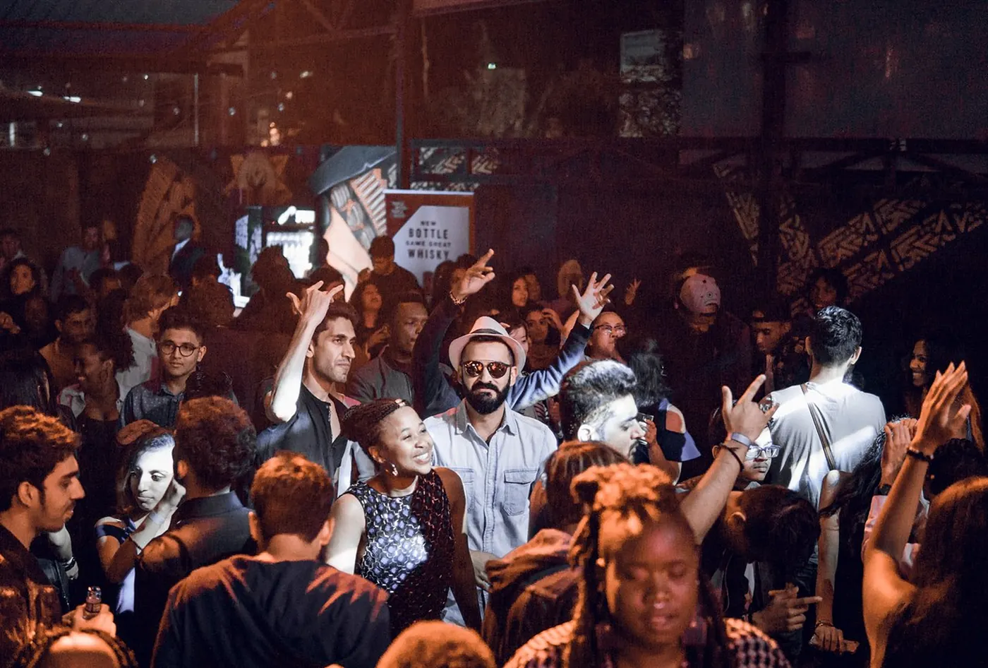 A crowded dancefloor of people with raised arms in warm light