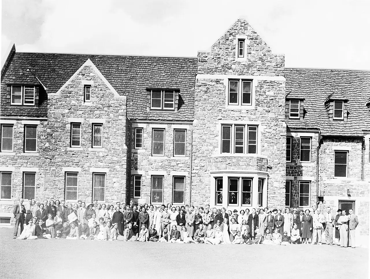 A black-and-white photograph of a stone building with people in front