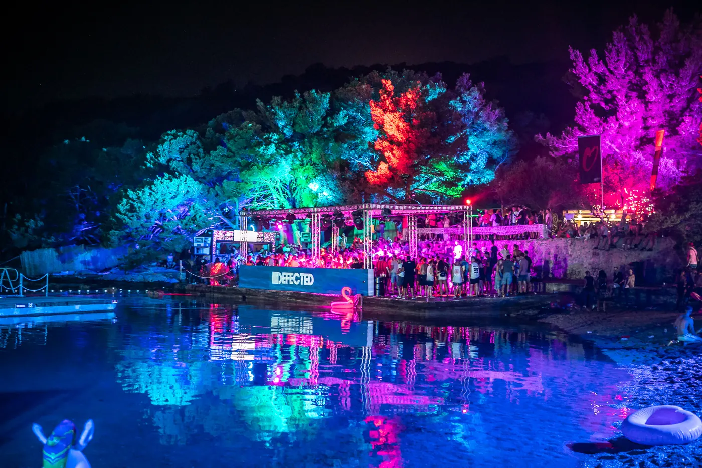 Trees and a waterside stage lit blue, green and pink at night