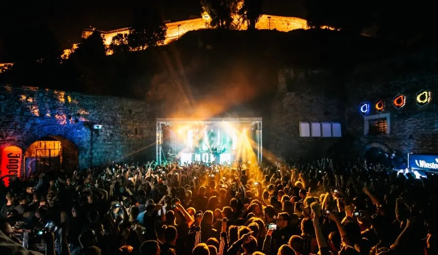 A crowd in front of a lit stage at night inside the fortress