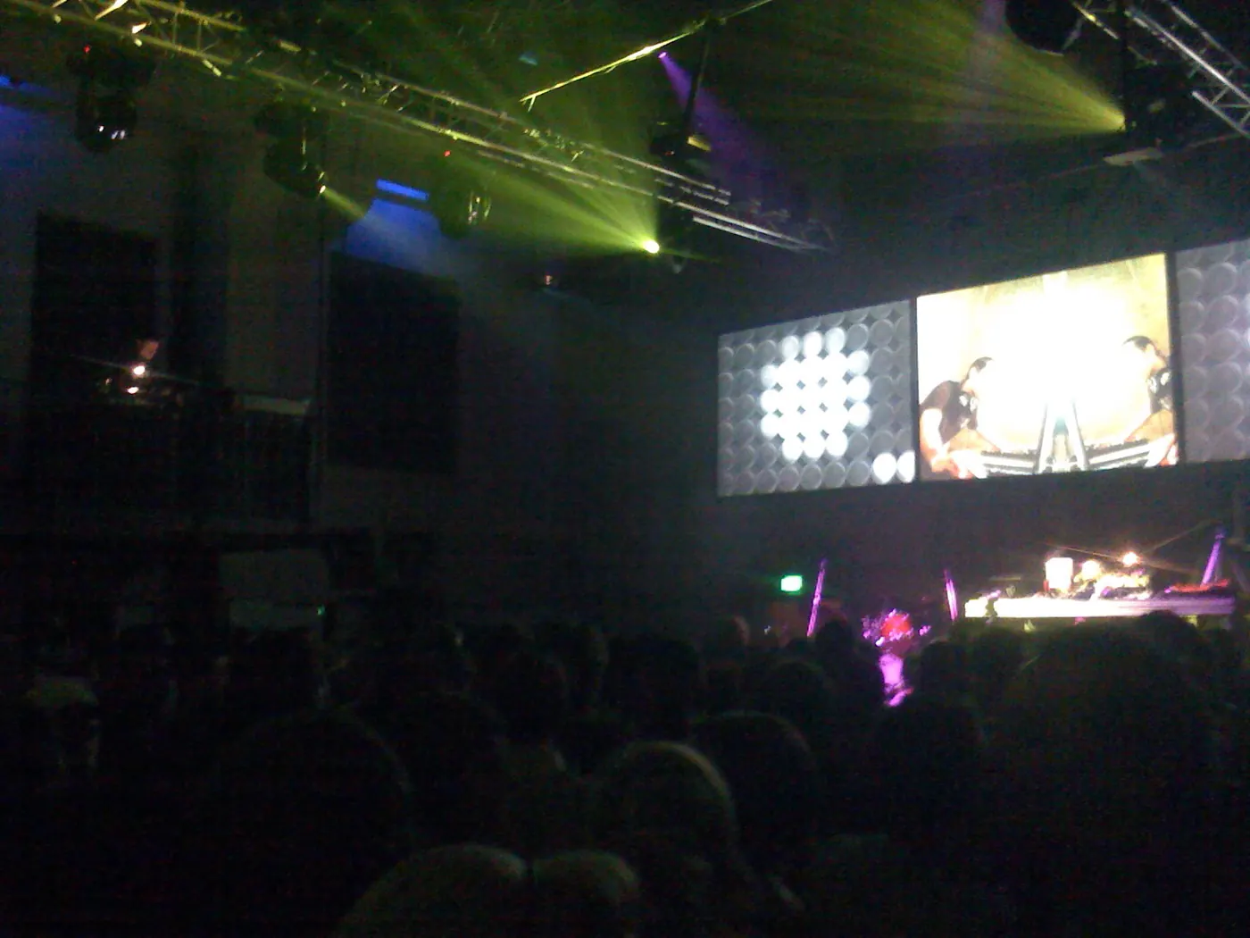 A screen and stage lights above a dark crowd at a concert in Berghain