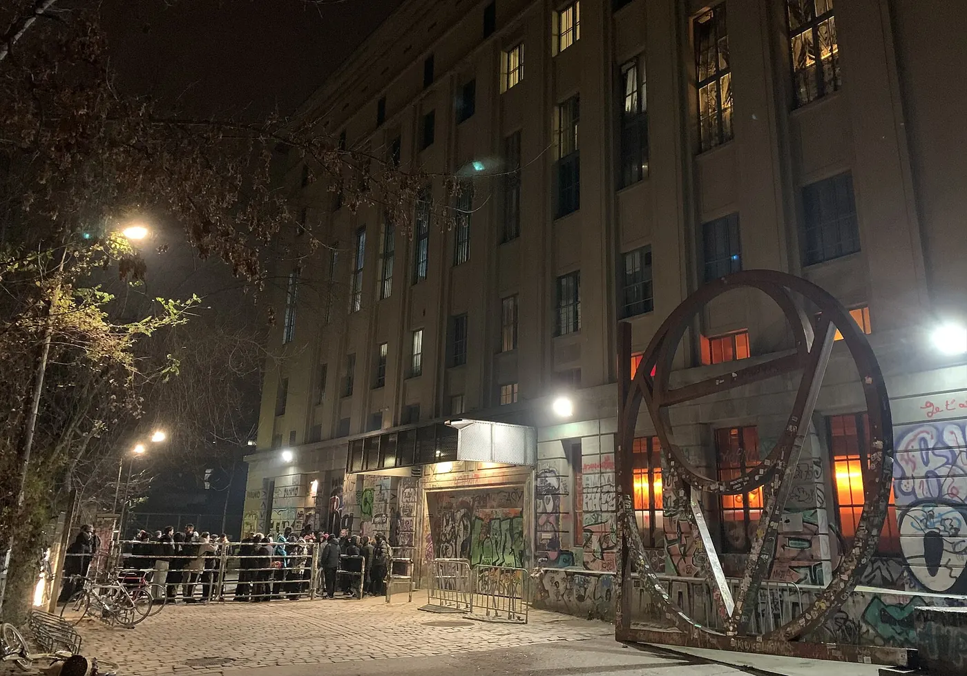 The Berghain building at night, with a large wheel sculpture and warm lights