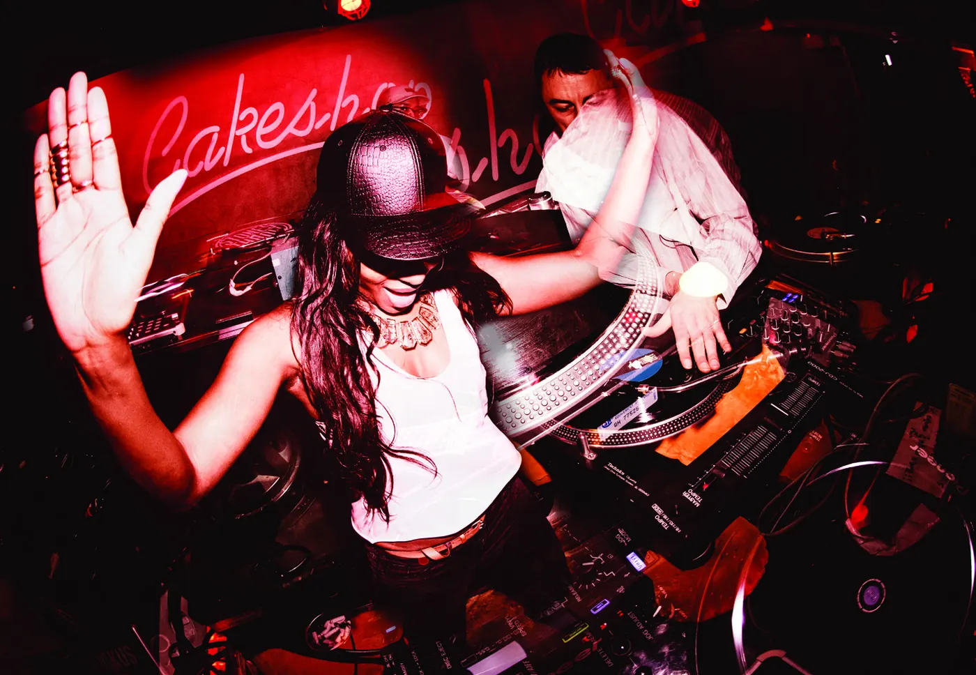 A DJ with a raised hand at the decks under red light