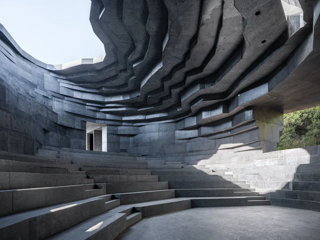 Stepped concrete seating curving up under a rough skylight