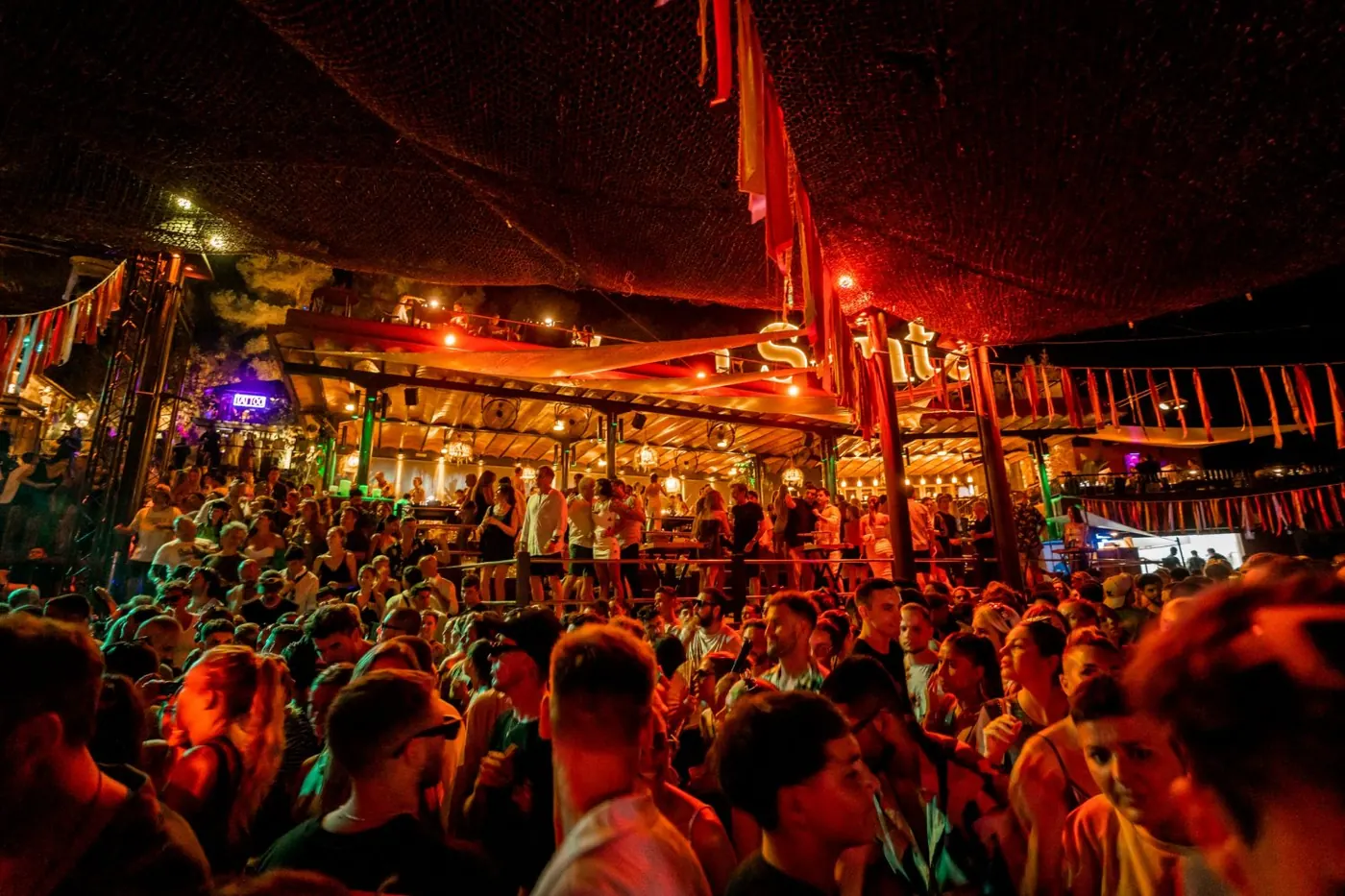 Crowd and stage under red and orange lighting at Cova Santa