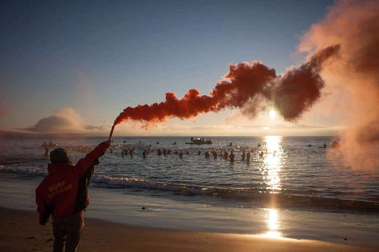 A person holding a red flare on a beach at sunset