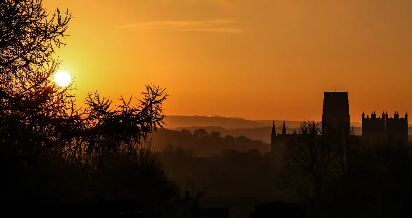 The towers of Durham Cathedral in silhouette against an orange sunrise sky