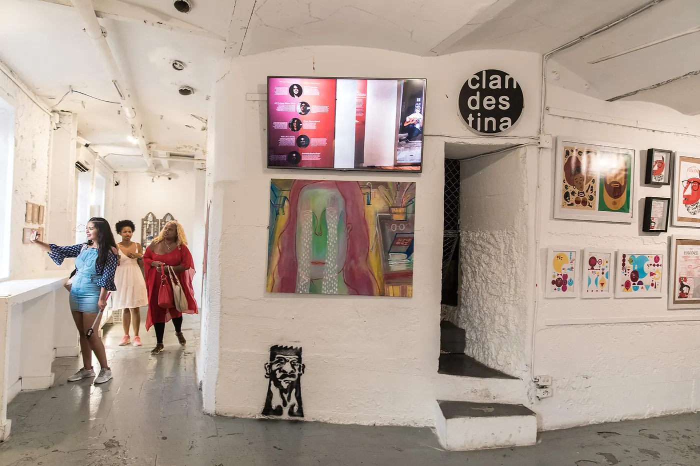A white gallery room with art on the walls and visitors