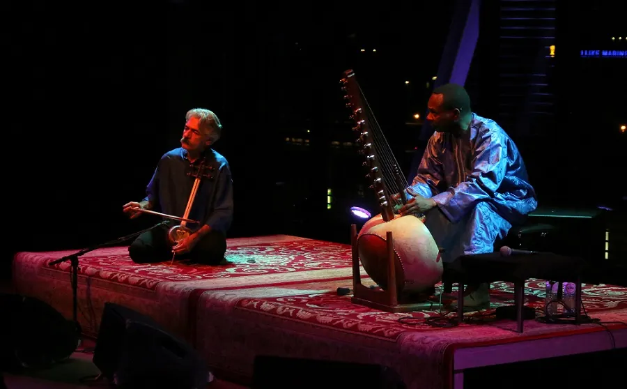 Two musicians playing kora and lute on a low stage
