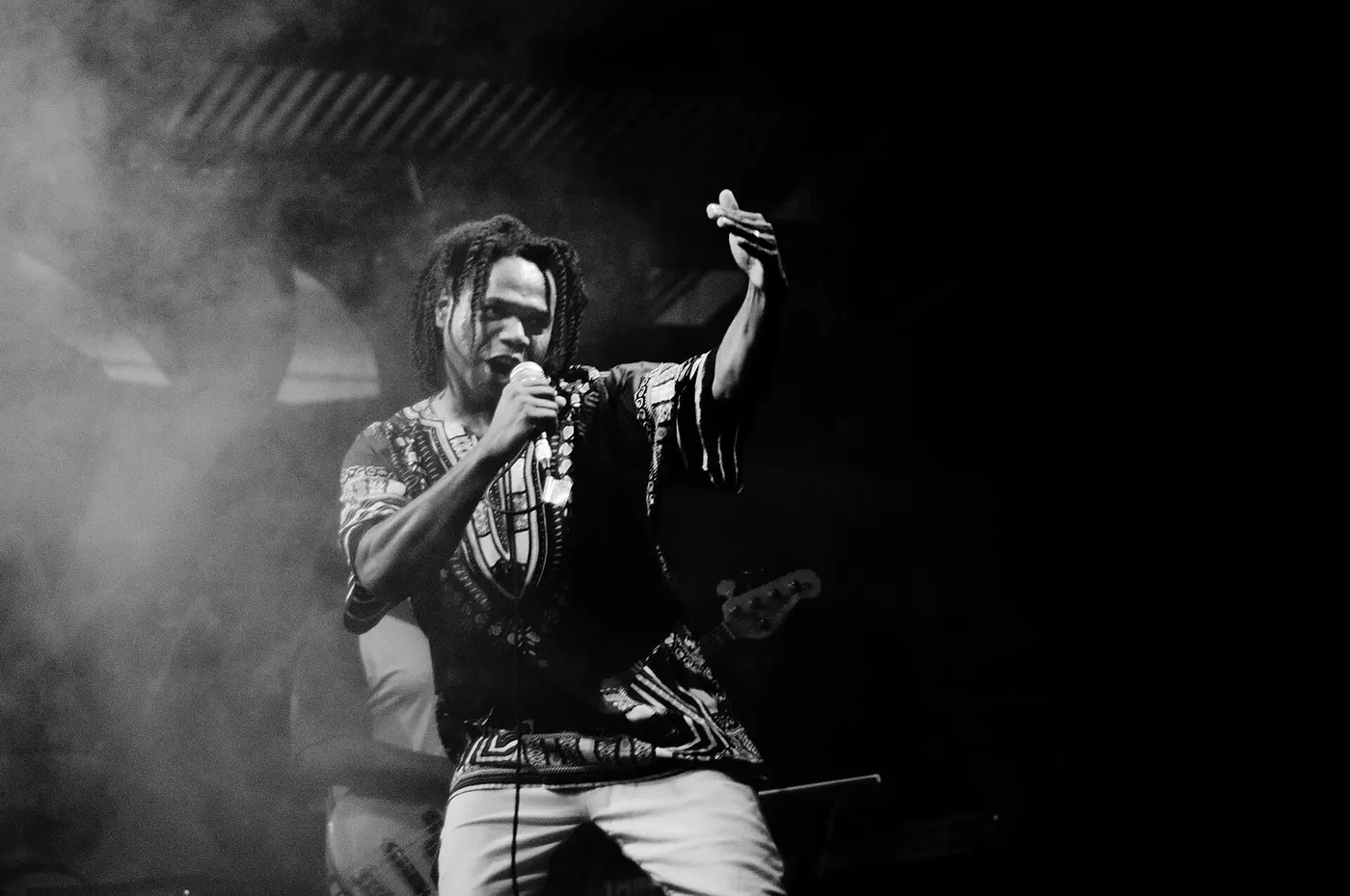 A black-and-white shot of a performer with an arm raised in stage haze