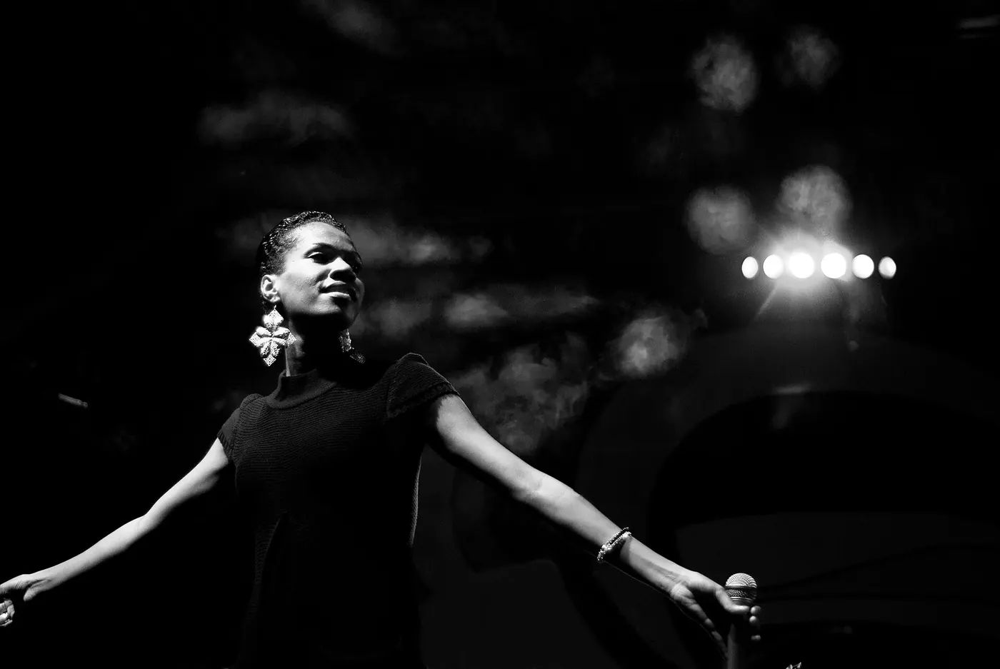 A black-and-white shot of a performer with arms spread wide in stage light