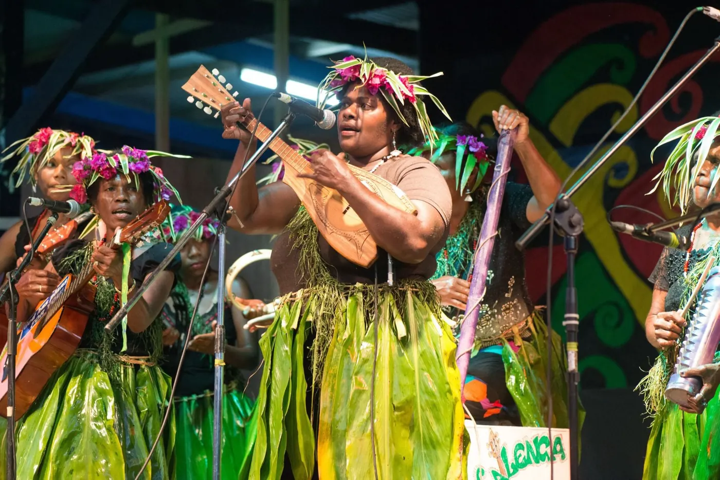 Women in grass skirts playing ukulele and bass on stage