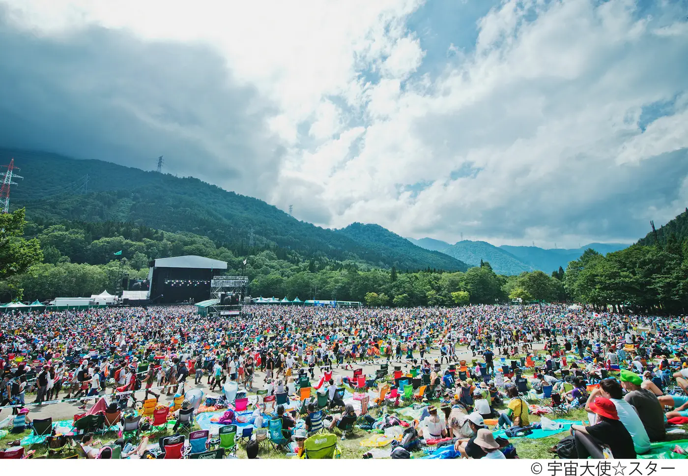 A sprawling festival field in a wooded valley under a cloudy sky