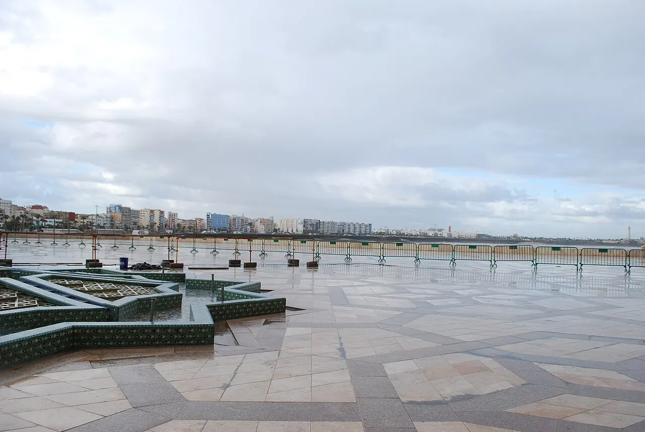 The wet stone plaza in front of the mosque, with the city skyline beyond