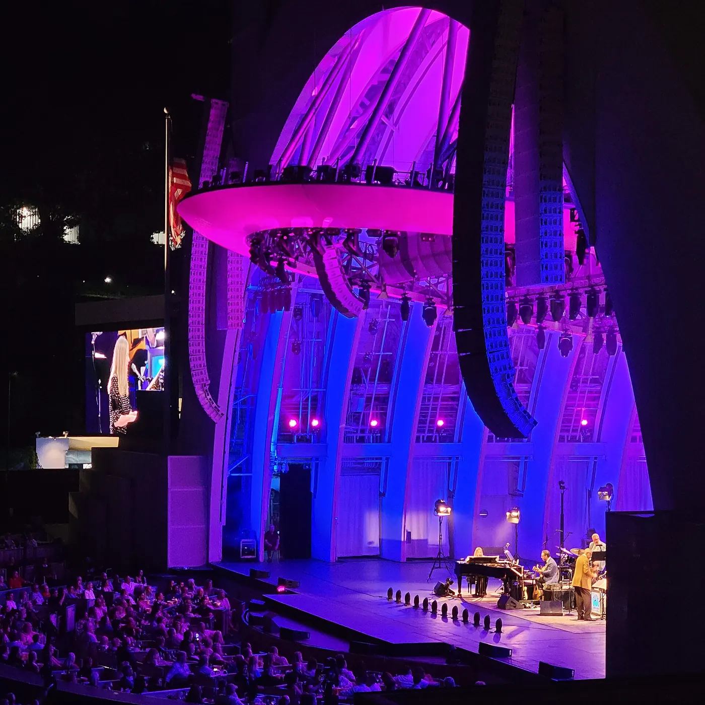 A jazz quartet on the Hollywood Bowl stage bathed in magenta and blue light, with boxes of listeners at lower left