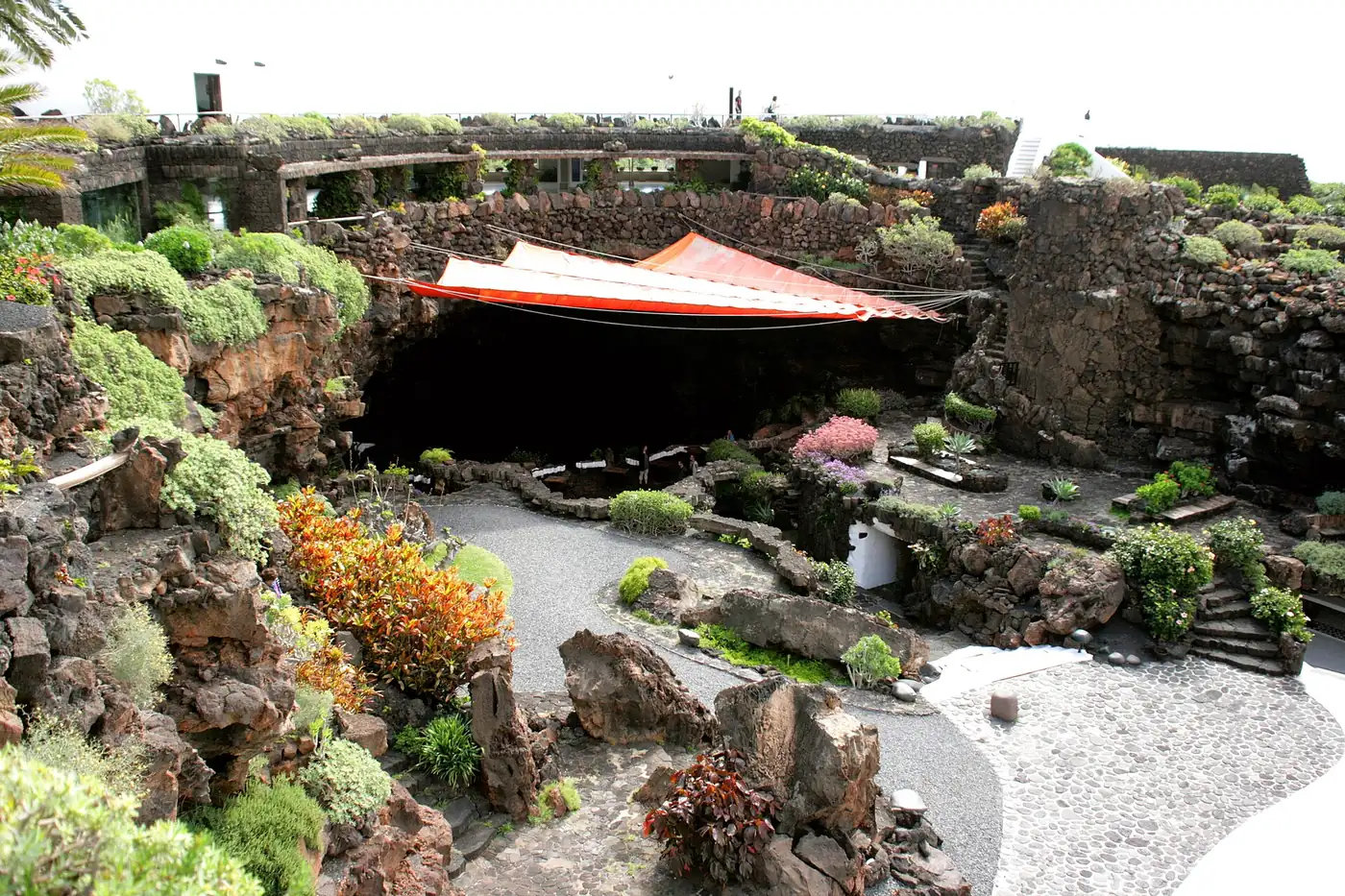 The Jameo Grande courtyard: a lava rock garden with a red awning over a cave mouth, with terraces and white walls above