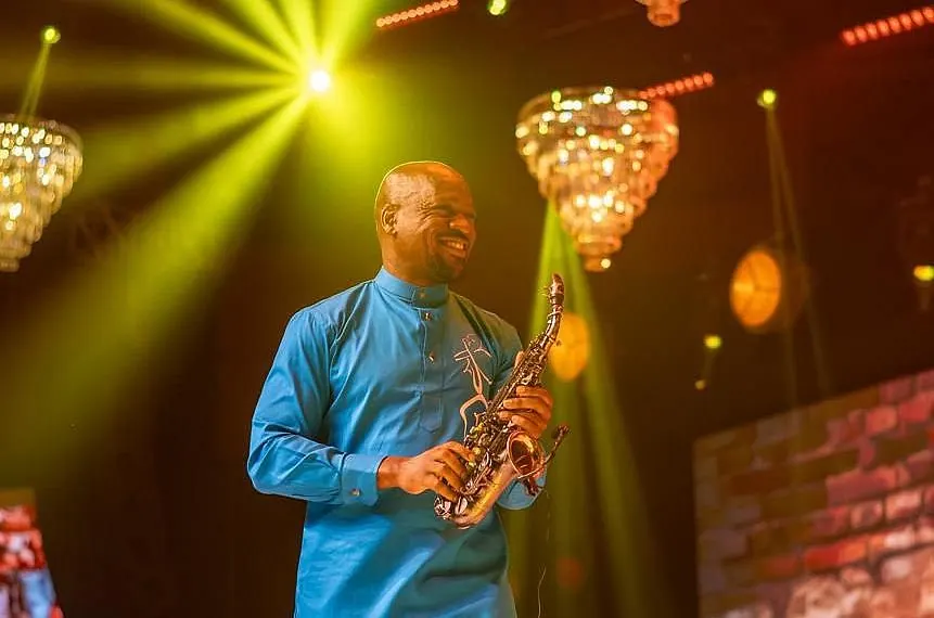 A saxophonist in a blue shirt under yellow stage lights