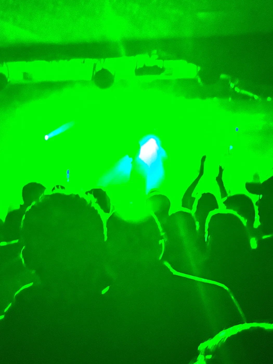 Hands raised under a wash of green stage light and haze in the concert room at King Street Social Club