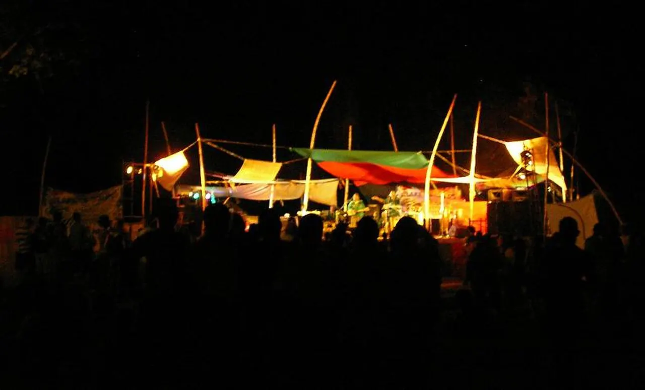 A dark night scene with small lit tents and the silhouettes of a crowd
