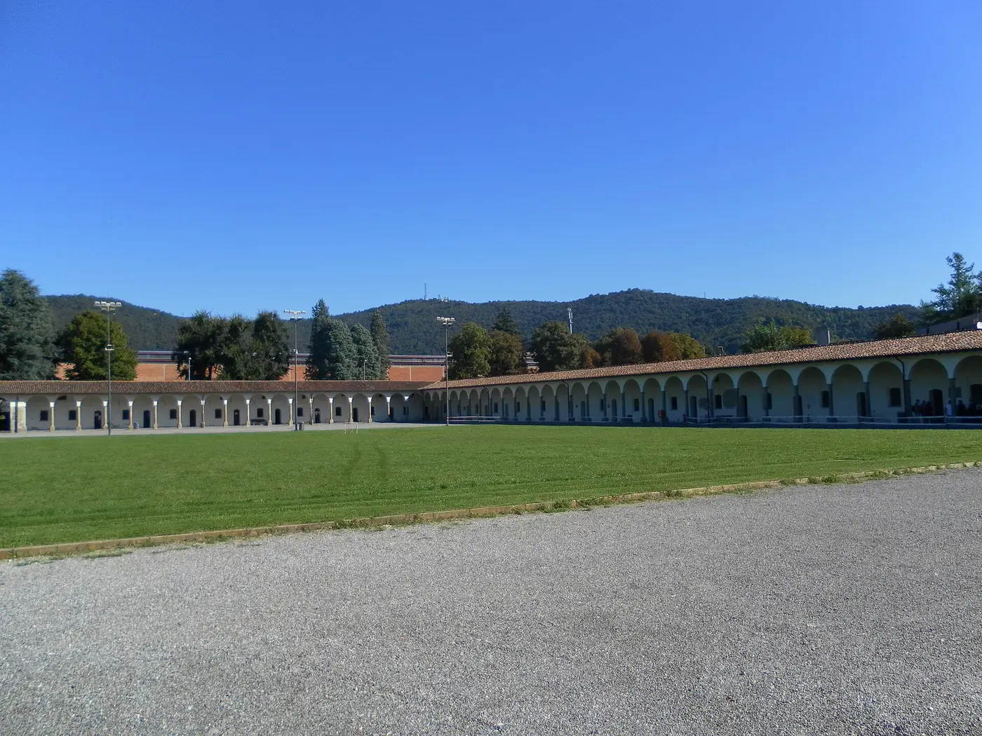The long arcade wall across a gravel path and lawn under a blue sky