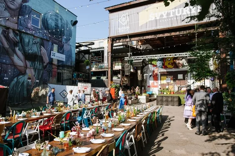A long banquet table in the courtyard between graffiti-covered buildings