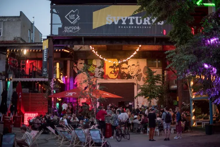 A busy courtyard bar with a lit sign and coloured lights