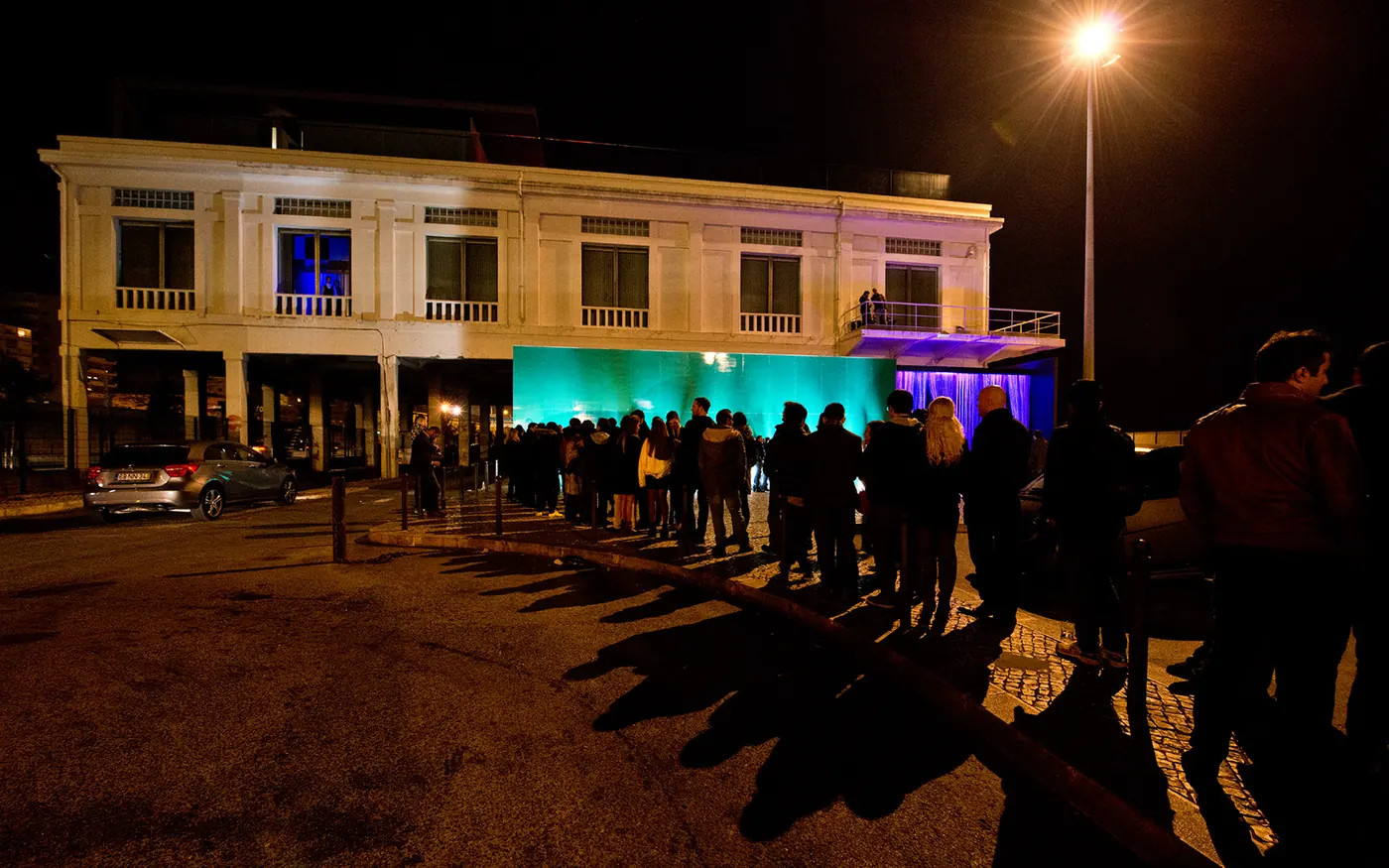 The Lux Frágil building at night with a queue outside and teal lighting