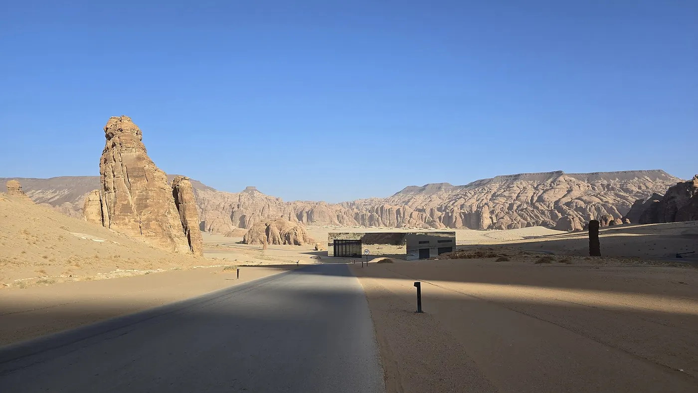 A road leading into the Ashar Valley with Maraya's mirrored box small on the horizon among sandstone pillars and cliffs