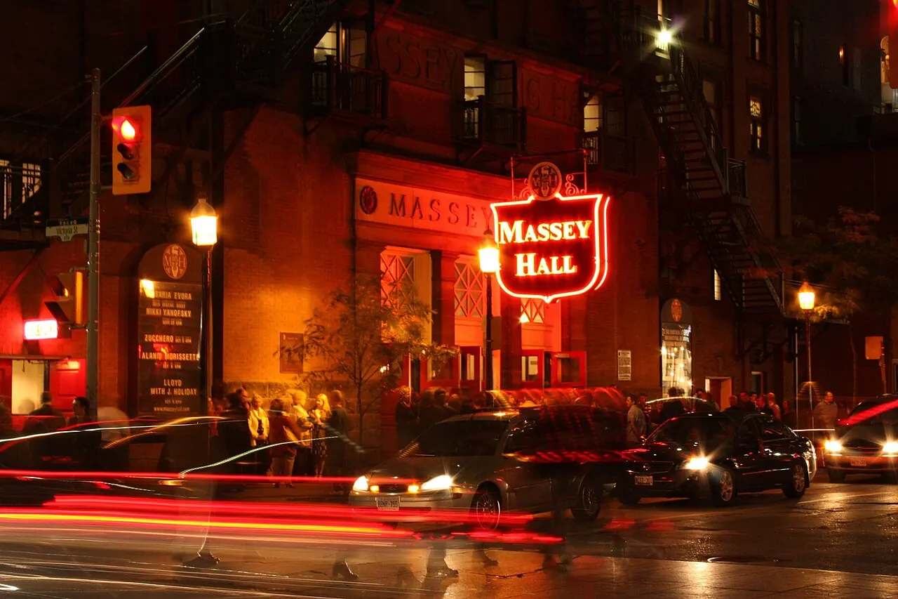 Massey Hall's lit sign at night with streaks of car lights