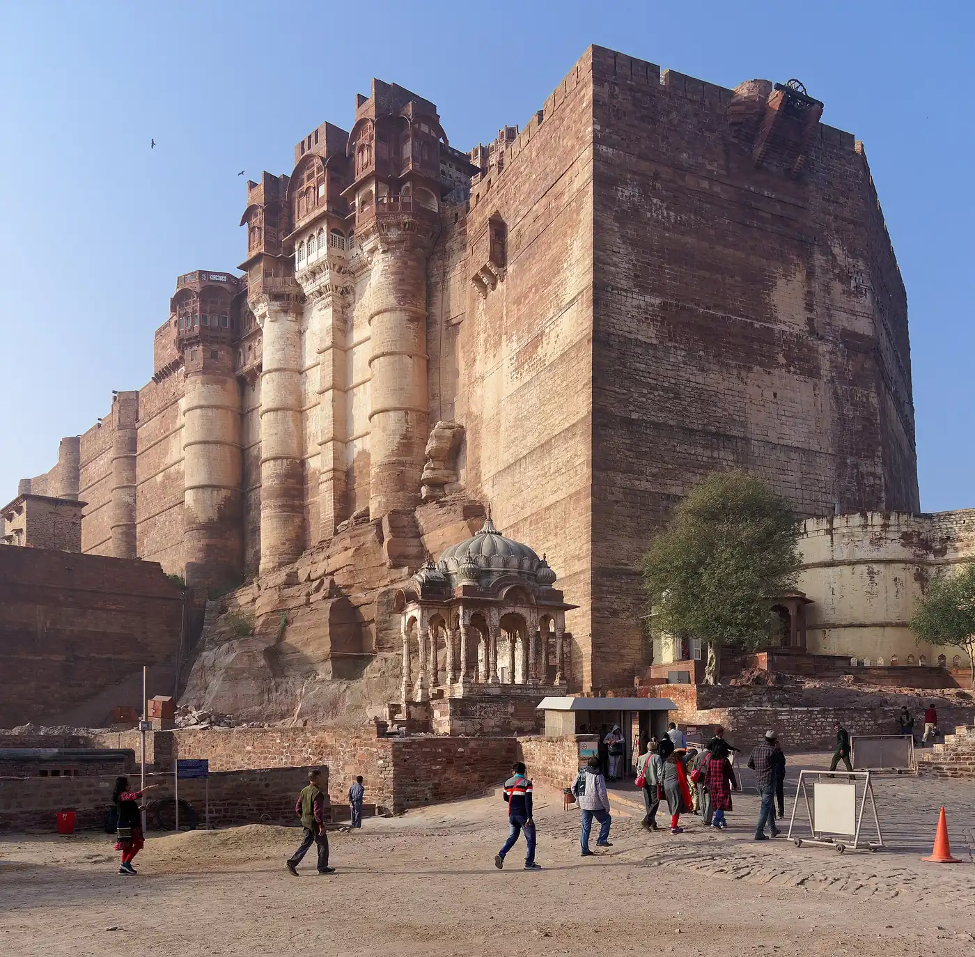 Mehrangarh Fort's towering sandstone walls and carved balconies rising above the approach, with visitors walking below