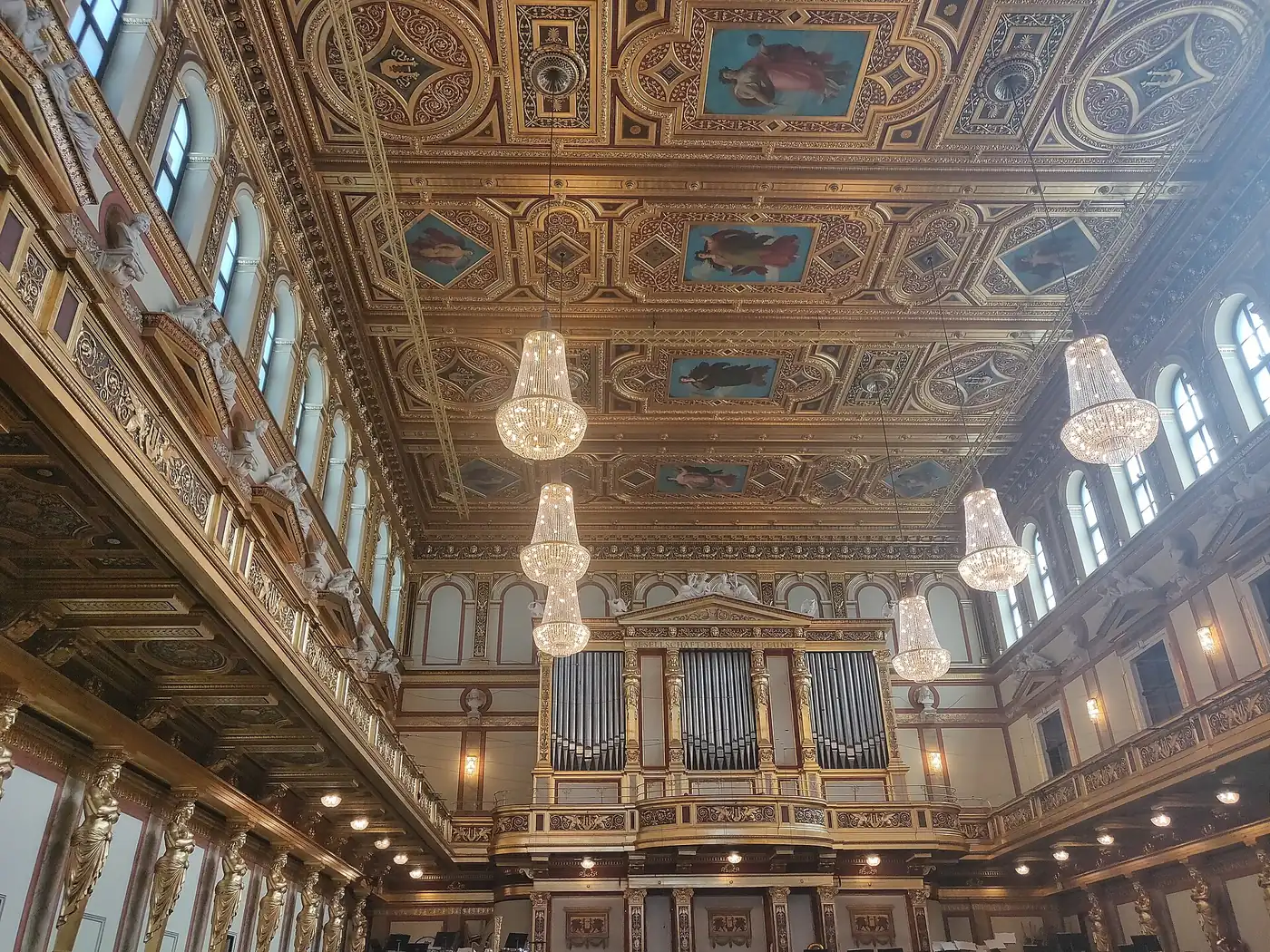 Looking up at the Golden Hall ceiling: painted panels, gold coffers, crystal chandeliers, arched windows and the organ at the far end