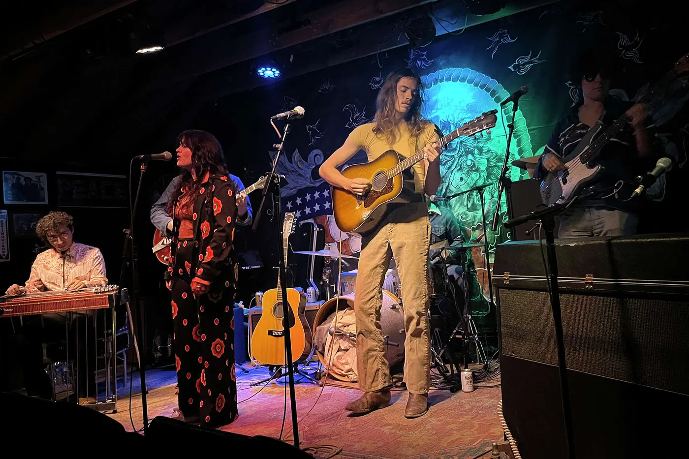 A guitarist and band playing in a dim, blue-lit room