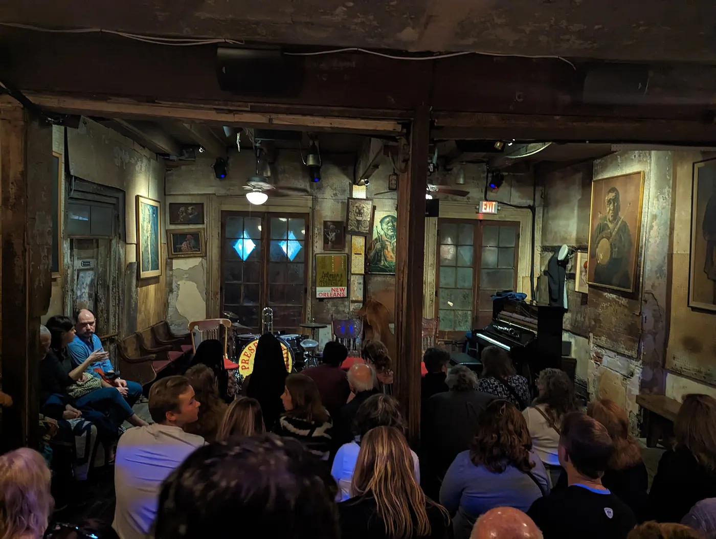 An audience on benches and the floor in the timber-beamed, peeling-plaster room at Preservation Hall before a set begins