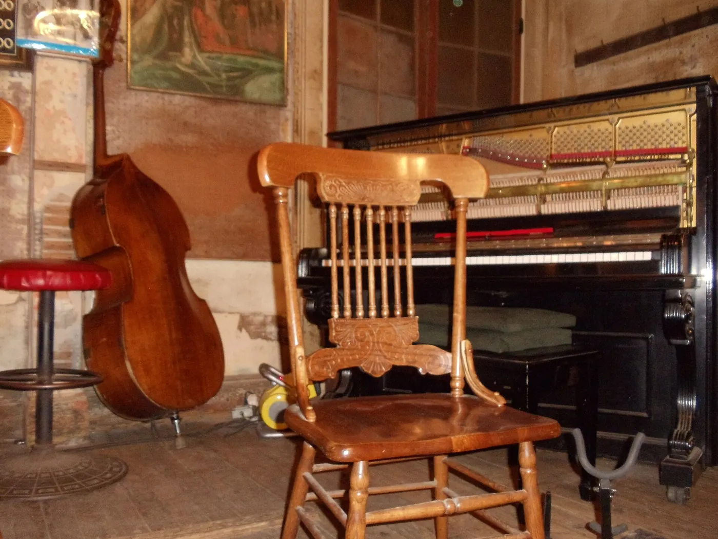 A wooden chair, an upright piano and a double bass on the bare boards of the Preservation Hall stage, walls worn to plaster