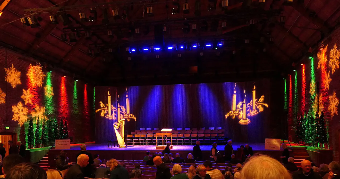 Snape Maltings Concert Hall set for a Christmas concert, with a harp on stage, projected candles and snowflakes on the brick walls