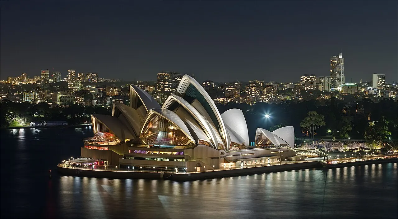The Opera House sails lit at night across the harbour