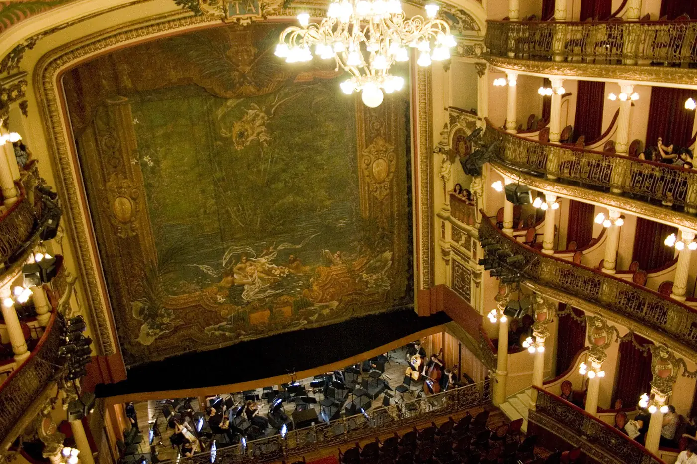 Looking down from the upper tiers of Teatro Amazonas to the painted curtain, a chandelier and an orchestra below