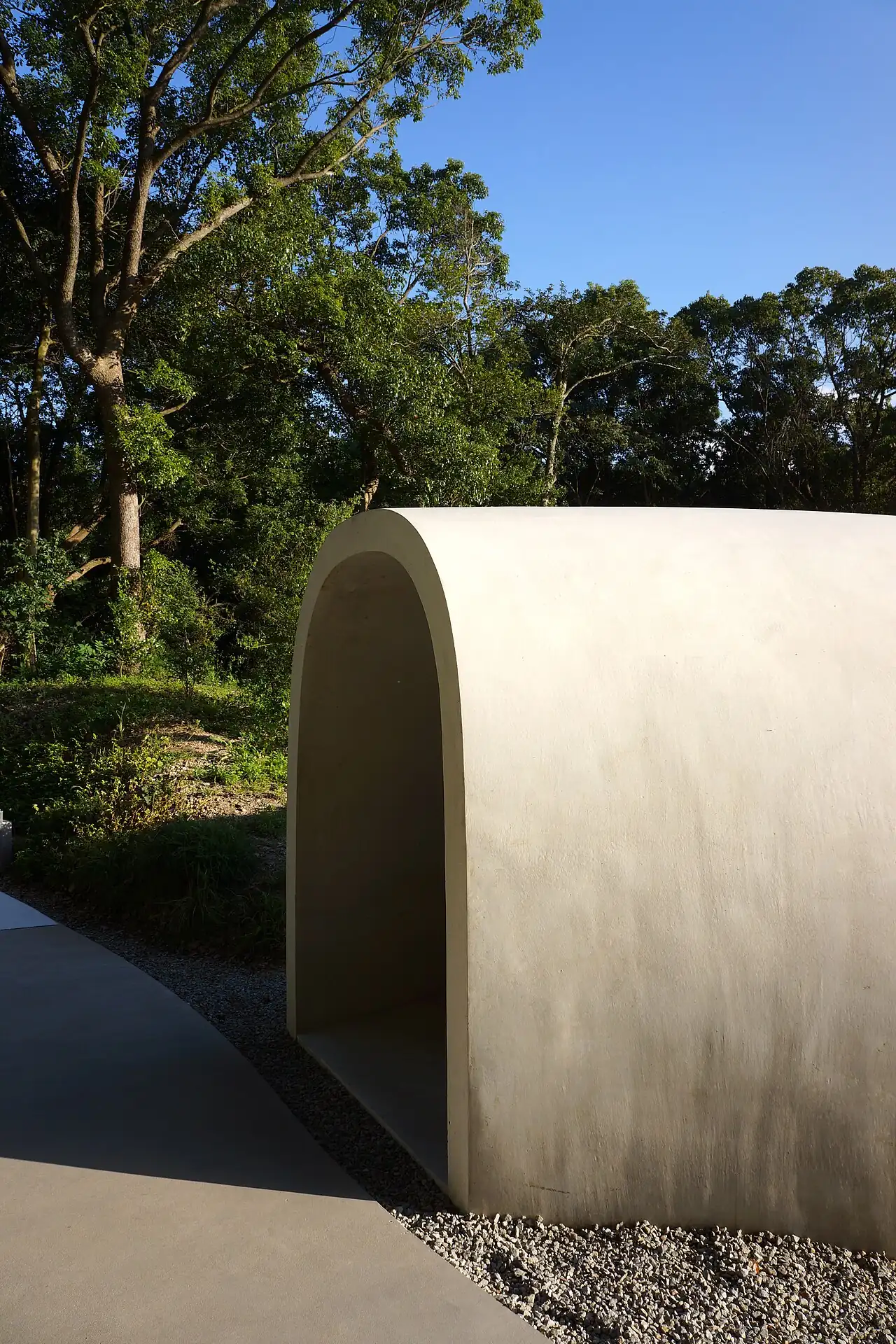A curved white wall against green trees