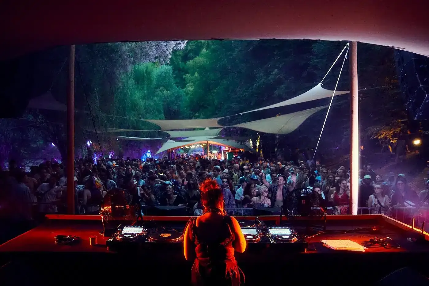 A crowd under a canopy in front of a stage lit in red