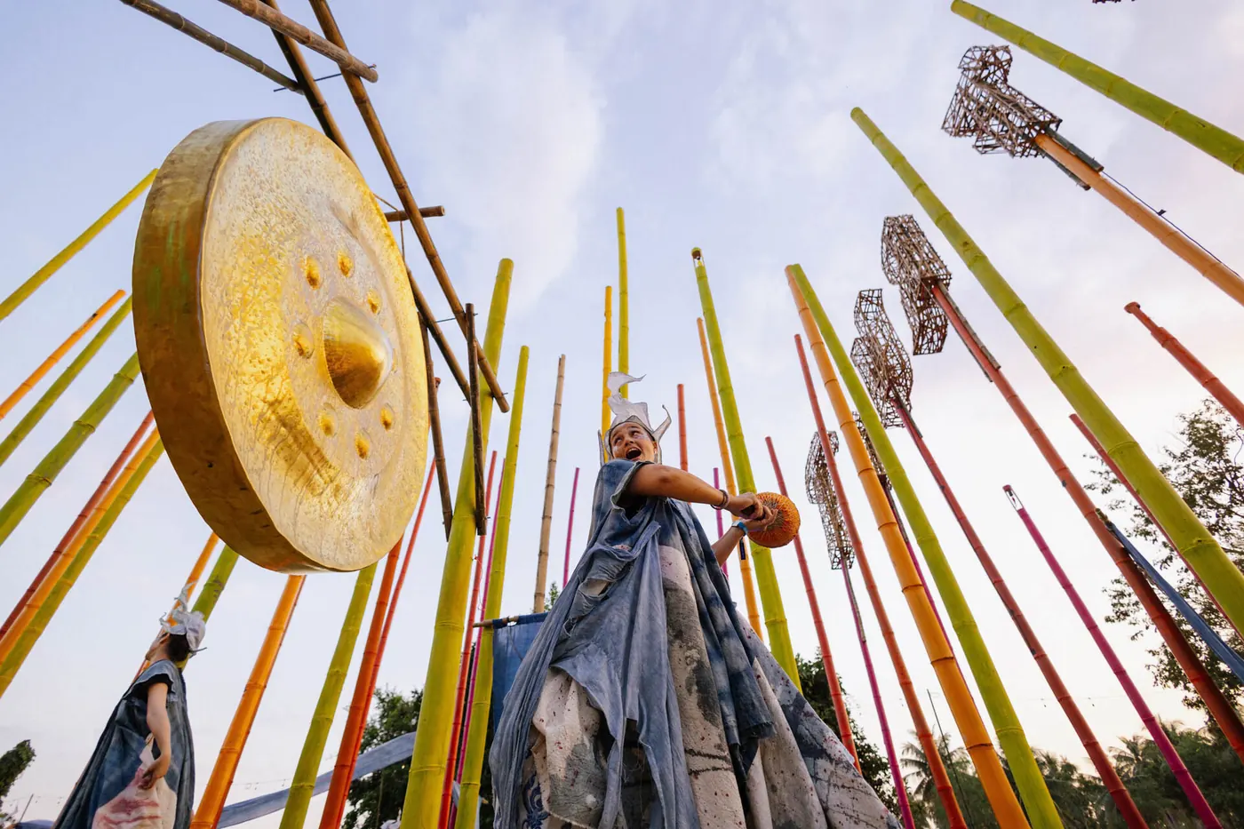 A performer among tall yellow poles and a large gong