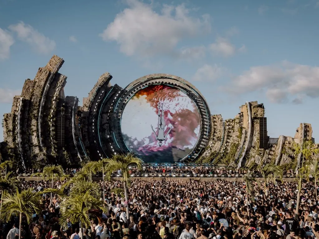 A crowd in front of a sculpted stage with a circular mirror, in the jungle