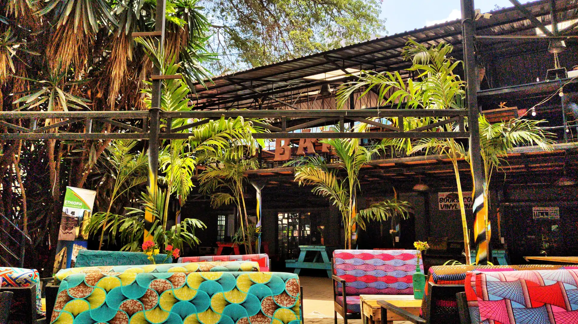A courtyard bar with palms, hanging lights and colourful seating