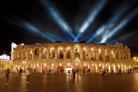 The Arena di Verona lit at night with searchlight beams in the sky