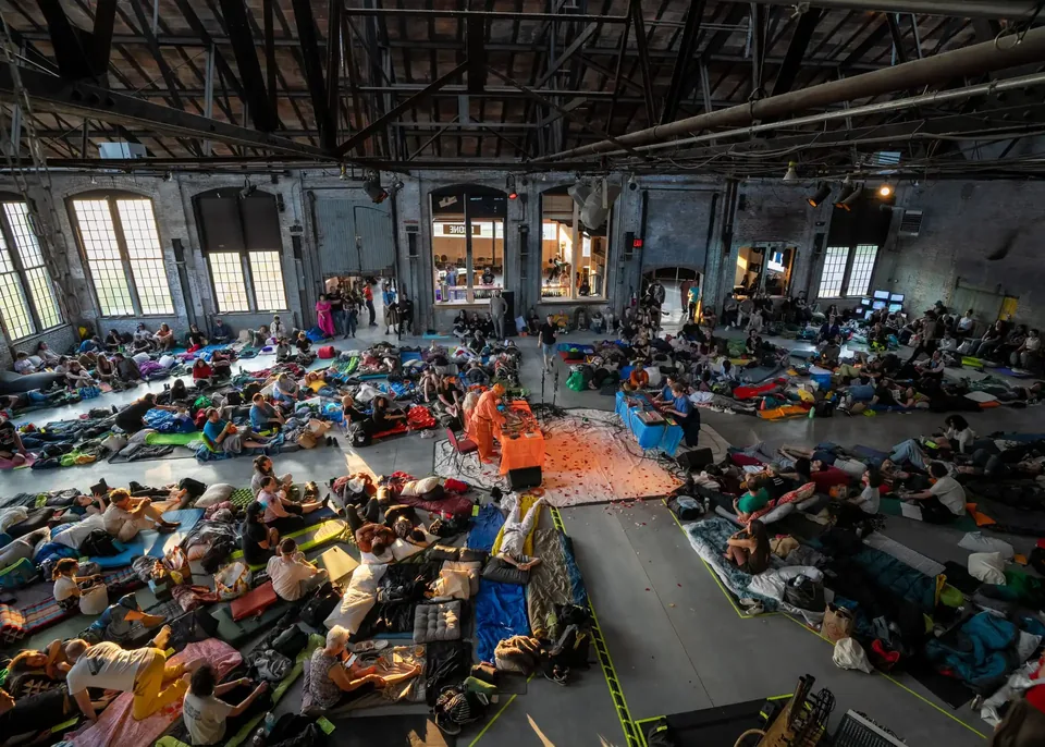 Crowds lying and sitting on the floor of a large brick warehouse hall at Basilica Hudson