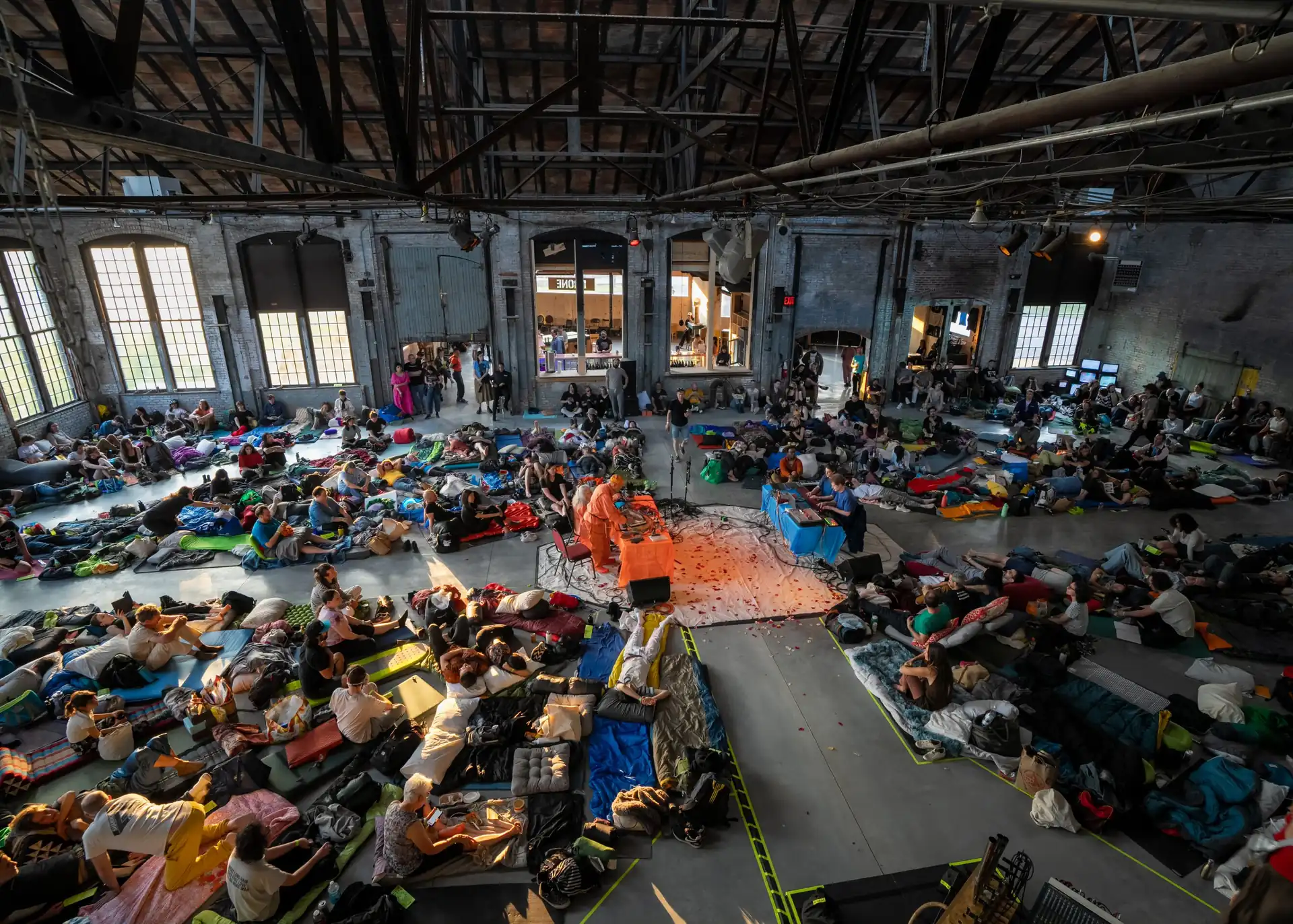 Crowds lying and sitting on the floor of a large brick warehouse hall at Basilica Hudson