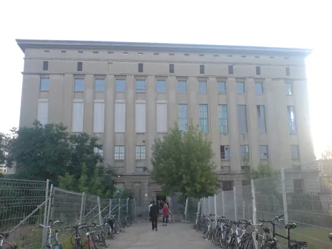 The pale concrete facade of Berghain seen from a fenced path