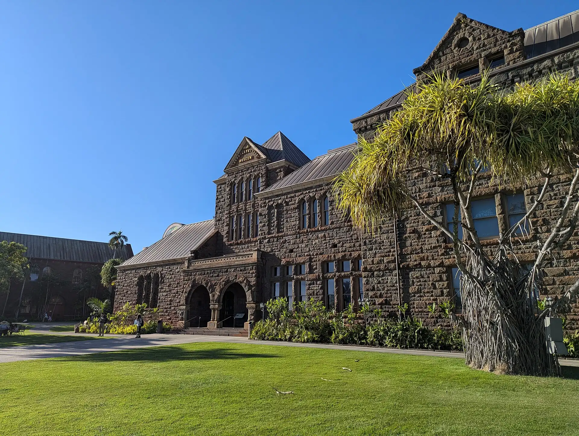 The stone Bishop Museum building on green grass under a blue sky