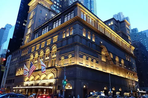 The illuminated tower of Carnegie Hall at night among New York skyscrapers