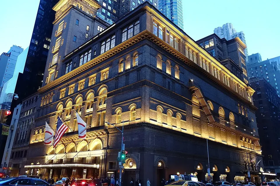 The illuminated tower of Carnegie Hall at night among New York skyscrapers